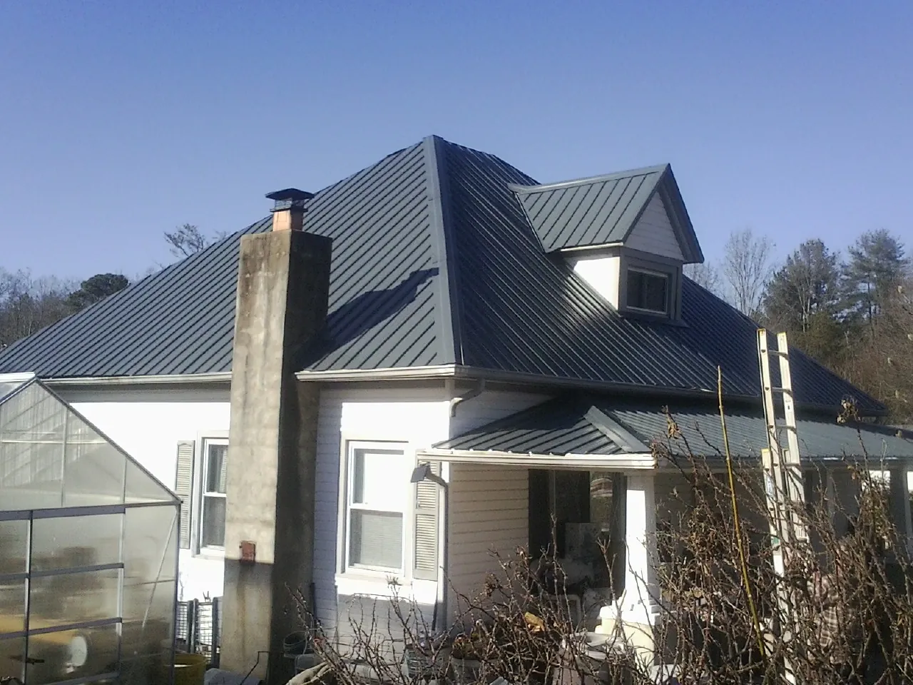 Dark blue standing seam metal roof on a white farmhouse with dormer — Slate & Tile Roof Repair by Roofing Brothers in Udell