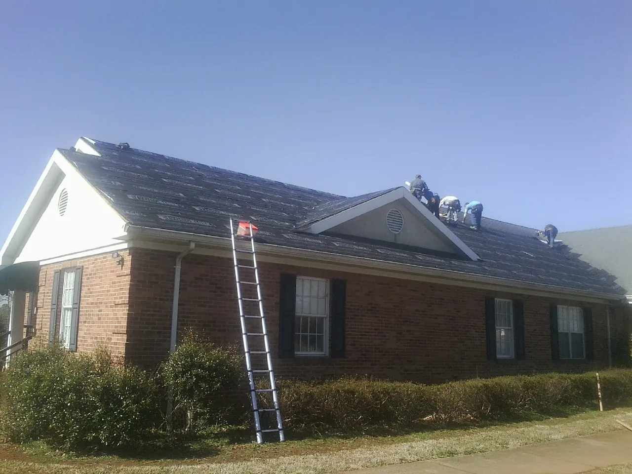 Crew tearing shingles off a brick ranch roof with a ladder set — Emergency Roof Repair work by our crew in Udell