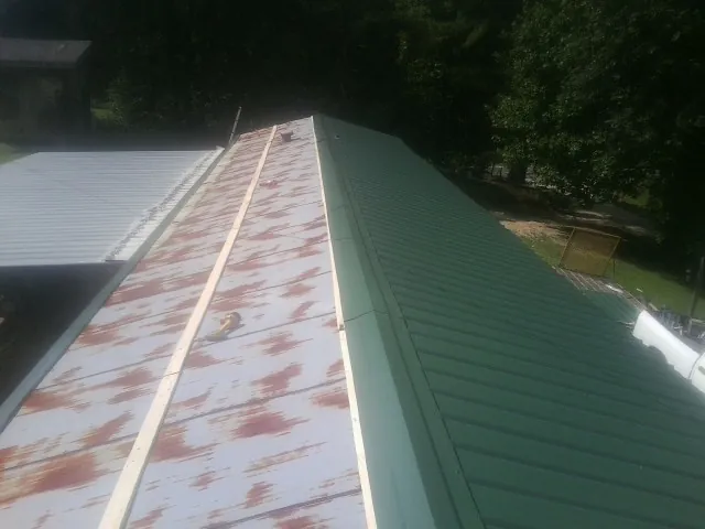 Old rusted panels beside newly installed green metal roofing — Wind Damage Roof Repair by Roofing Brothers in Udell