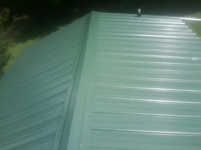 New green metal panels meeting at the ridge of a roof — Flat Roof Repair work by our crew in Udell