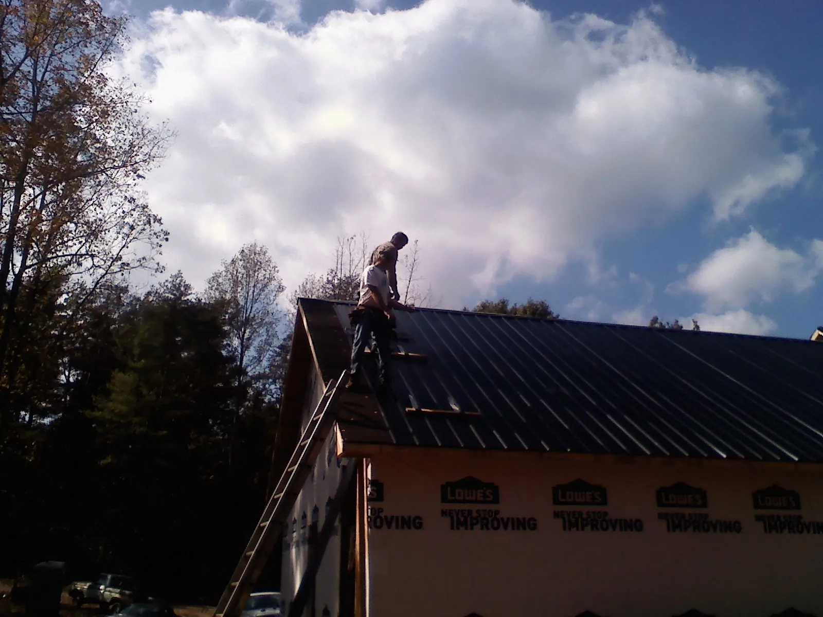 Roofer fastening dark metal panels high against a cloudy sky, from a Roof Inspection job in Udell