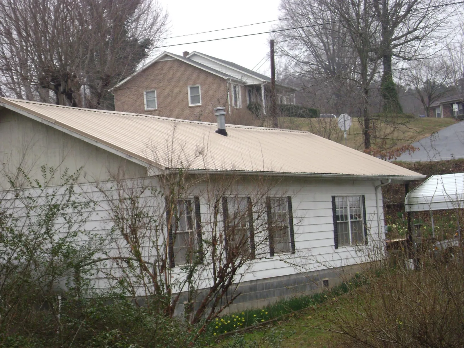 Tan metal roof on a white sided house set into a hillside — Commercial Roofing by Roofing Brothers in Udell