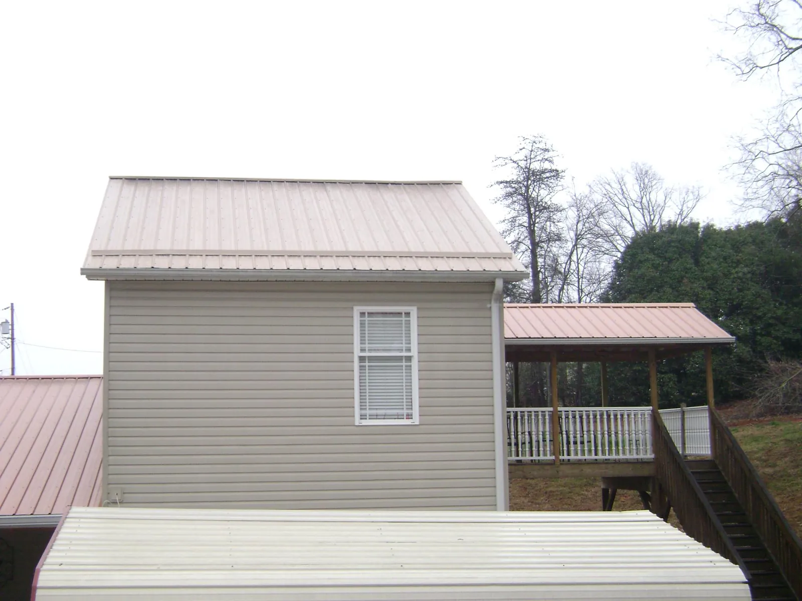 Tan metal roofs on a two story addition and attached porch, from a Roof Replacement job in Udell