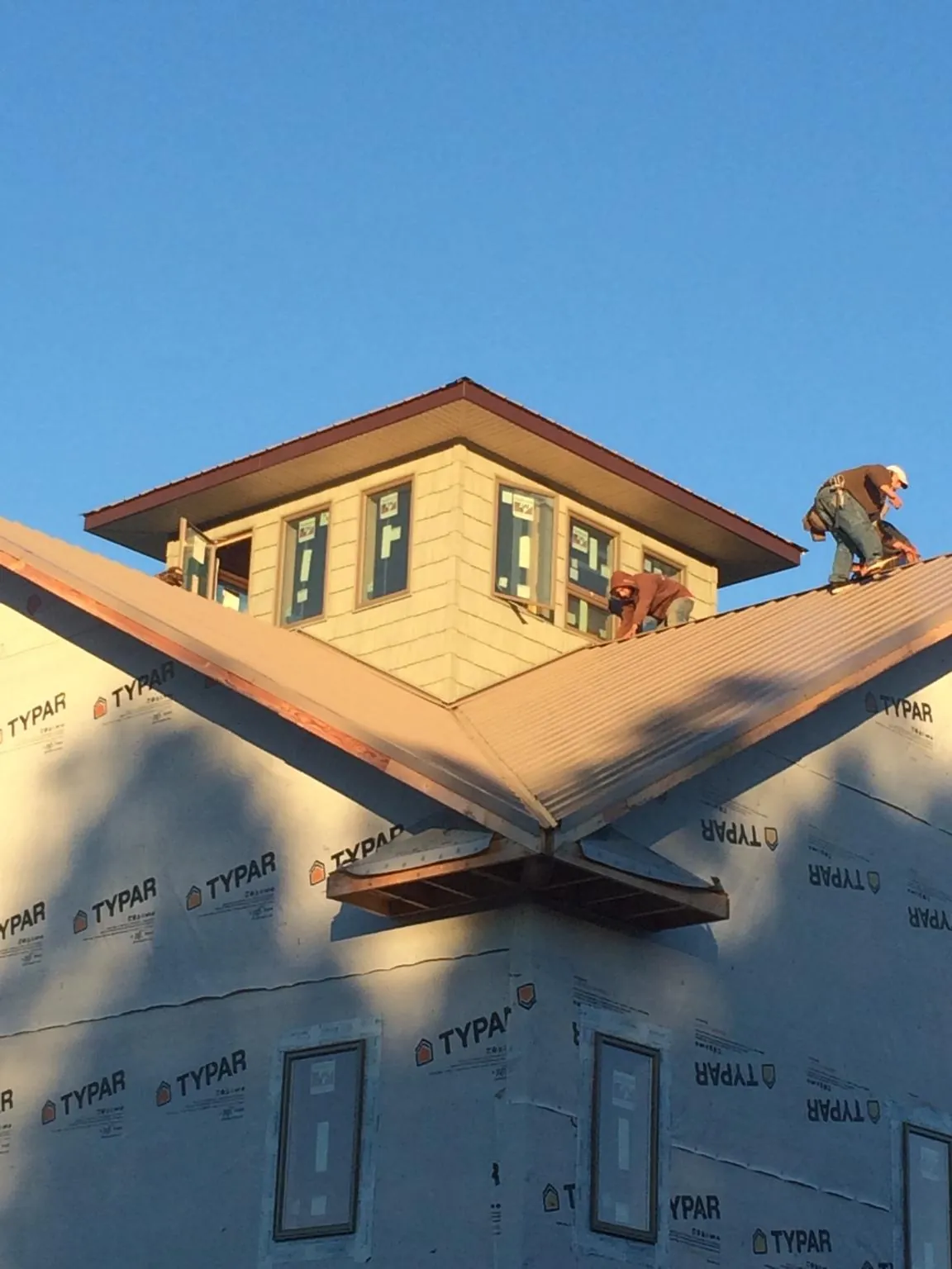 Roofers working around a rooftop cupola on a new metal roof at sunset — Roof Waterproofing in Udell by Roofing Brothers